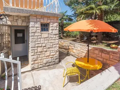 Die kleine Terrasse mit Tisch und zwei Stühlen, Sonnenschirm und dem Eingang zur Studio-Wohnung