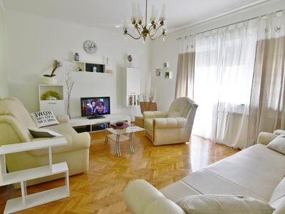 Das Wohnzimmer mit Schlafsofa, Couchtisch und Flachbild-Kabel-TV, Regale führt zum Balkon