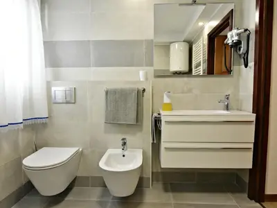 Das Badezimmer verfügt über ein Waschbecken mit Schrank und Spiegel, Haartrockner, Bidet und Toilette.