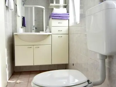 Das Badezimmer hat ein Waschbecken mit Schrank und Spiegel, WC.