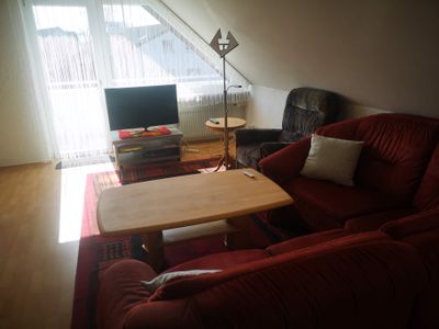 Wohnzimmer mit Couch, Fernseher, Sessel und Balkon