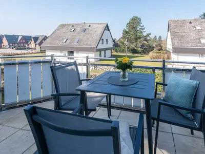 auf dem Westbalkon von Ferienwohnung Carmen App. 12 stehen drei Stühle und ein Tisch mit Blumen