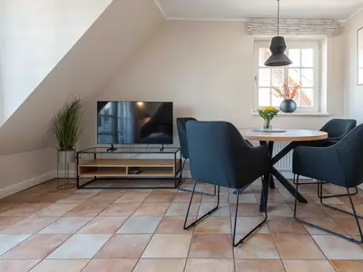 im Wohnzimmer der Ferienwohnung Carmen App. 12 steht ein runder Tisch mit vier Stühlen und links ein TV Board