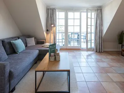 im Wohnzimmer von Ferienwohnung Carmen App. 12 steht ein Sofa, Sofatisch und die Balkontür ist offen
