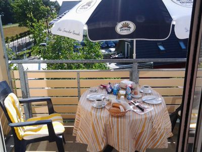 Balkon mit Esstisch, Bestuhlung, Sonnenschirm und einen Blick auf die Deichpromenade