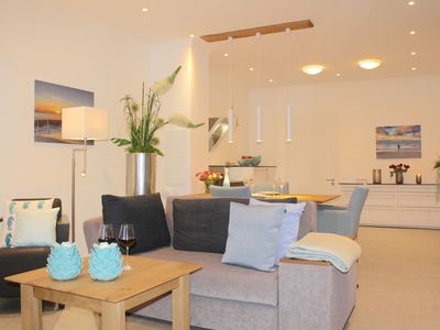 Wohnbereich mit Sessel, Couch und Blick auf die offene Küche mit Esstisch und Bestuhlung