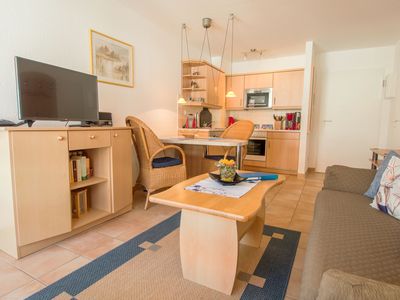 Wohnbereich mit Sofa, Couchtisch, Sideboard und TV mit Blick in die offene Küche