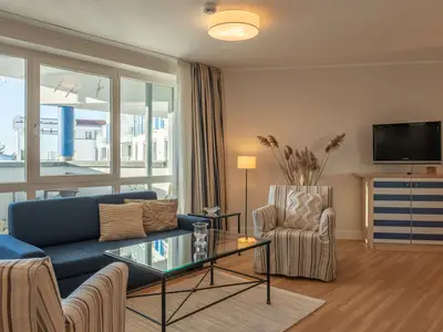 Ferienwohnung Kranichtanz Aparthotel Zingst - Blick ins helle Wohnzimmer mit einer Couch, zwei Sesseln und einem TV