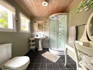 Grosses Badezimmer mit Erlebnis-Dusche, WC, Frisiertisch und Rollcontainer. Zwei Fenster mit Vorhängen.