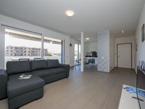 Wohnzimmer mit Zugang zum Balkon, Schlafsofa und offener Küche