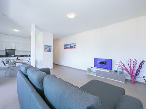 Wohnzimmer mit Fernseher, Schlafsofa und offener Küche