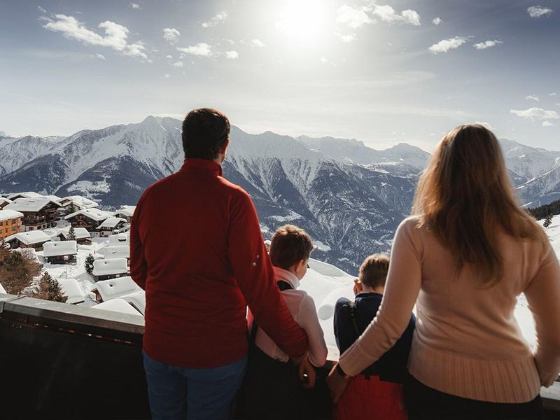 Familie geniesst Walliser Bergpanorama vom Apartment Balkon im Winter
