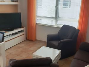 Wohnzimmer mit Sofa, zwei Sesseln, Esstisch und Bestuhlung sowie Sideboard und TV