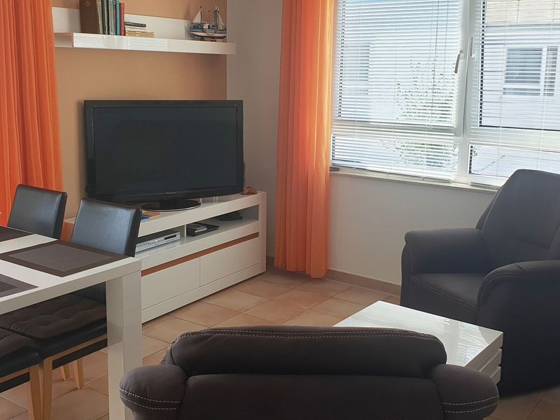 Wohnzimmer mit Sofa, zwei Sesseln, Esstisch und Bestuhlung sowie Sideboard und TV