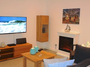 Wohnbereich mit Sofa, Sessel, Couchtisch, Elektrokamin und Sideboard mit TV