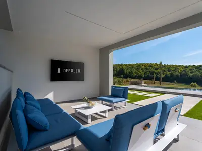 Überdachter Bereich mit einer Loungeecke, einem Flachbildfernseher, ein paar Liegestühlen mit Sitzsäcken und einer Bar