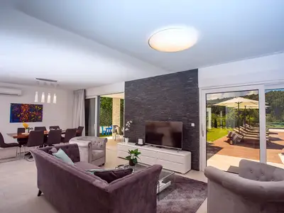 Ein Wohnzimmer mit TV und Ausgang zu einem Pool und einem Essbereich im Freien.