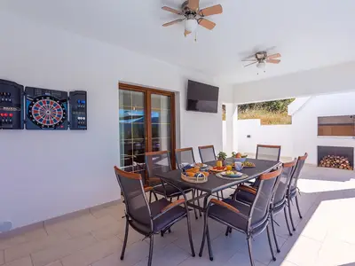 Überdachter Essbereich für 8 Personen im Freien mit einem Fernseher, Darts zum Spaß und einem traditionellen Grill daneben