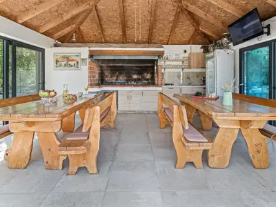 Eine voll ausgestattete Sommerküche mit traditionellem Grillplatz, Esstischen, einem Fernseher und einer separaten Toilette.