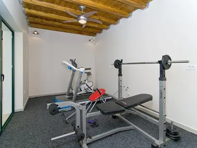 
Fitnessraum mit Laufband, Bank mit Gewichten und Heimtrainer.