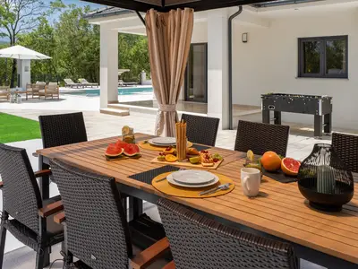 Ein überdachter Außen-Essbereich mit einem großen Tisch und einem Holzkohlegrill für Mahlzeiten im Freien.
