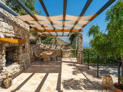 Covered and not overlooked outdoor dining area with a stone table and a traditional barbecue (woods, charcoal) next to it, all in front of the kitchen
