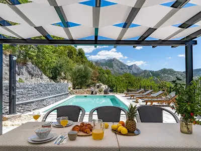 Ein Essbereich im Freien für 6 Personen, mit einem traditionellen Grill, einem Kühlschrank und 4 Liegestühlen, Sonnenschirm