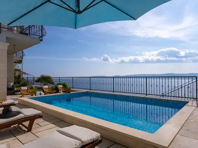 Erleben Sie vollkommene Entspannung in der Villa S&A mit Blick auf das offene Meer vom Pool aus, der mit türkisfarbenen Fliesen und einem Sonnenschirm ausgestattet ist.