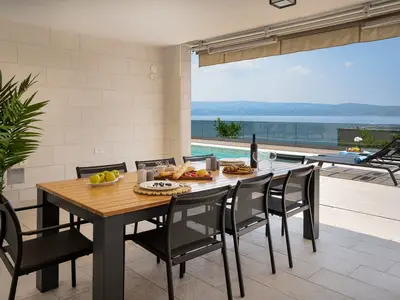 Covered outdoor dining area with BBQ and speakers, between pool and living area
