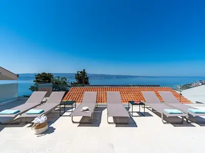 Ein Sonnendeckbereich mit 6 Liegestühlen, zusätzlich 6 Terrassenstühlen und dem Esstisch mit Sonnenschirmen
