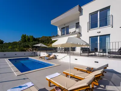 Es liegt oberhalb der Küstenstraße im Dorf Podstrana, umgeben von typischen mediterranen Pflanzen wie Pinien und Olivenbäumen
