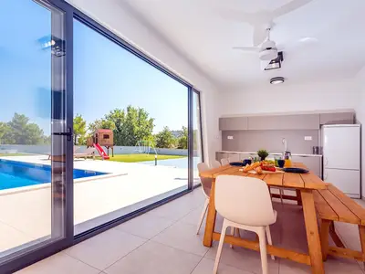 Eine voll ausgestattete Sommerküche mit TV, Kühlschrank, Grill und Essbereich für 10 Personen