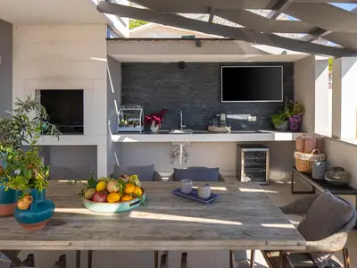  Ein Essbereich im Freien mit einem Esstisch für 8 Personen mit Grill, einem Fernseher und einem Kühlschrank 