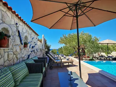 Ein gemütlicher Lounge-Bereich mit bequemen Kissen und Steinmauern lädt zum Verweilen am Pool ein, mit Blick auf das Meer in der Ferne.