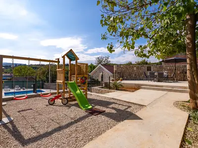 Unter einem Baum liegt ein Klettergerüst für Kinder mit Rutsche und Schaukel, das den jüngeren Gästen viel Spaß bietet.