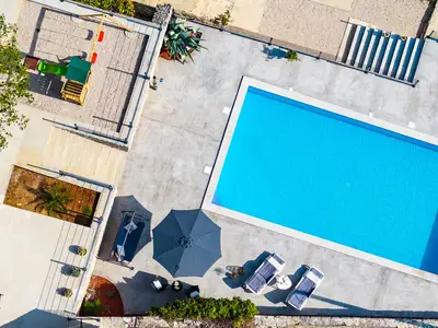 Diese Luftaufnahme zeigt den großen privaten Swimmingpool und den weitläufigen Außenbereich mit Sonnenterrasse, Lounge und angrenzendem Spielplatz.