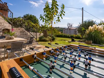 Der Spielbereich im Erdgeschoss erstreckt sich bis in den Außenbereich mit einem Tischfußballspiel auf einer charmanten Steinterrasse – perfekt für gesellige Stunden.