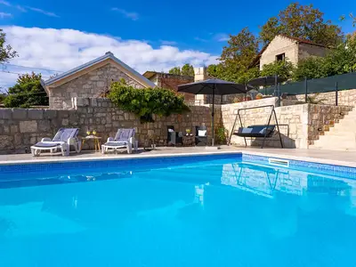 Vom Beckenrand aus bietet sich ein erfrischender Blick auf die terrassenförmig angelegte Sonnenterrasse mit Liegestühlen, Sonnenschirm und Schaukelstuhl sowie auf die rustikale Steinkonstruktion.