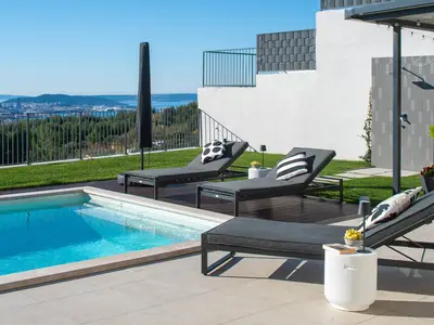 Sonnenterrasse mit bequemen Liegen mit Blick auf den Pool und die ferne Stadtlandschaft von Split und die Inseln.