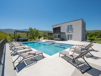 Moderne Villa mit großer Terrasse, beheiztem Pool und mehreren schattigen Loungebereichen im Freien.