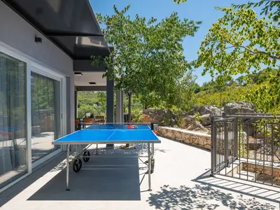 Schattige Terrasse mit Tischtennisplatte, ideal für Spiele neben Garten und Steinmauern.