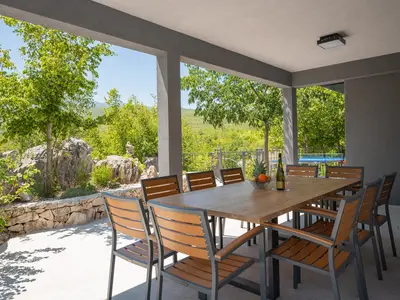 Überdachte Terrasse mit großem Esstisch, ideal für Mahlzeiten mit Blick auf den Pool.