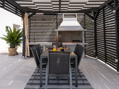 Überdachter Essbereich im Freien mit traditionellem Grill und einem Tisch für 8 Personen.
